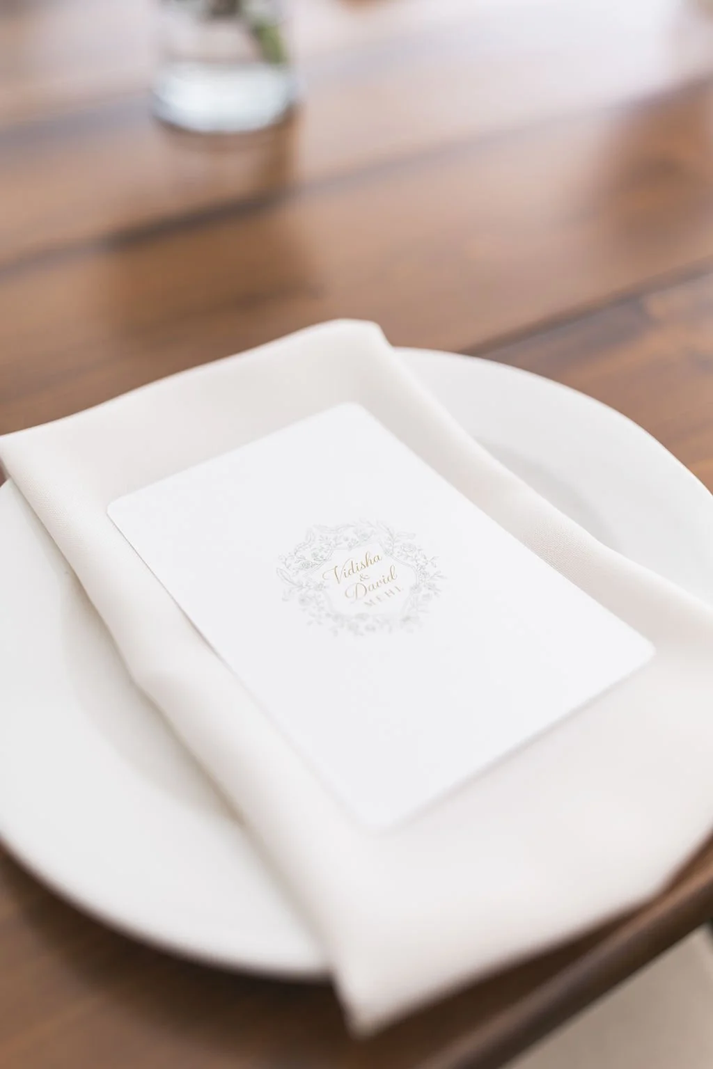 Wedding menu placed on a white napkin on a white plate, with a water glass in the background.