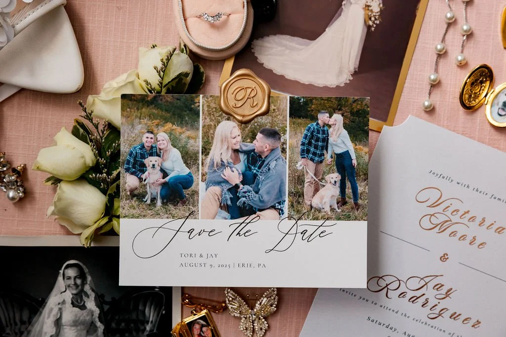 Wedding planning items including a 'Save the Date' card featuring photos of a couple and their dog, wedding invitation, jewelry, flowers, and other accessories on a pink surface.