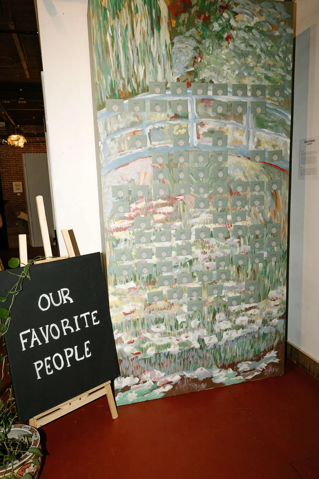 A large painted mural of a garden scene with white flowers, green foliage, and a bridge, with small cards or notes attached to it. A blackboard sign in front reads "Our Favorite People."