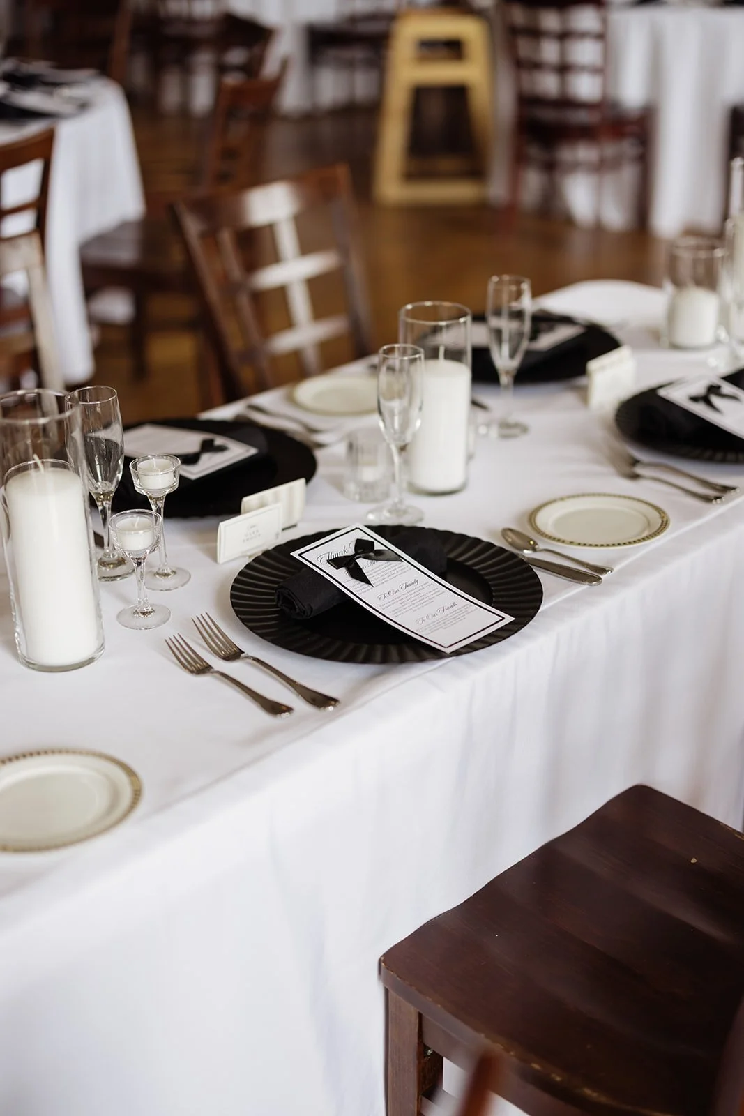 Elegant banquet table set for a formal event with white tablecloth, black and white themed place settings, candles, and glassware in a room with wooden furniture.