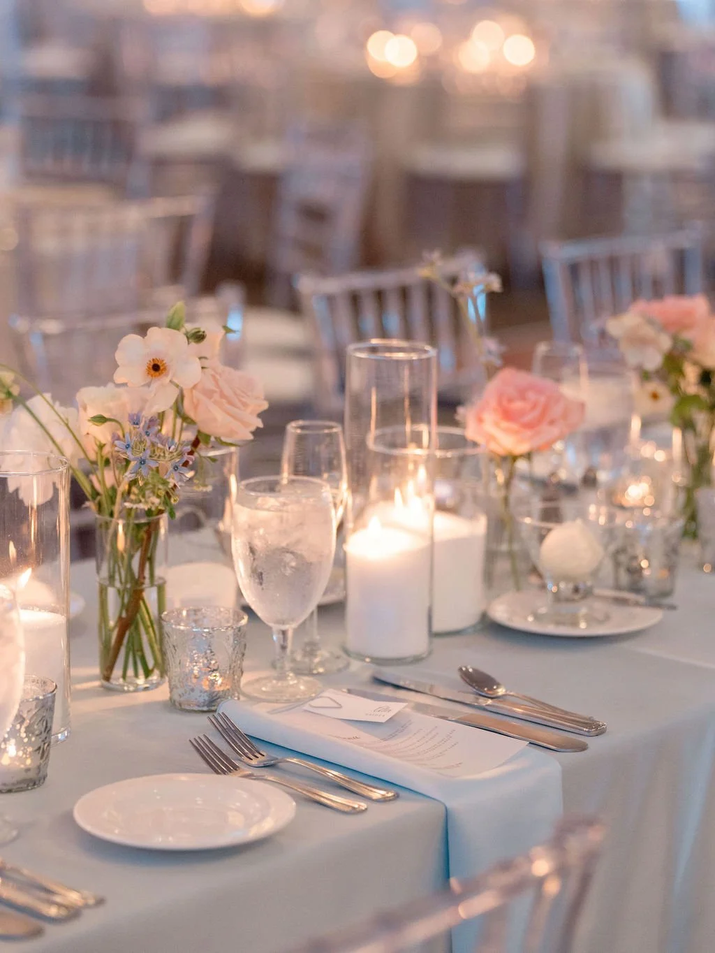 Elegant dining table decorated with pink and white flowers, candles, wine glasses, and place settings, set for a formal event or wedding reception.