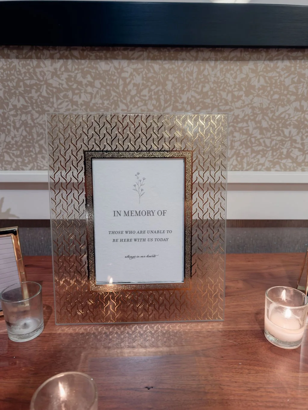 Memorial table with a framed sign on a wooden table, surrounded by small candles, in memory of those unable to be present.