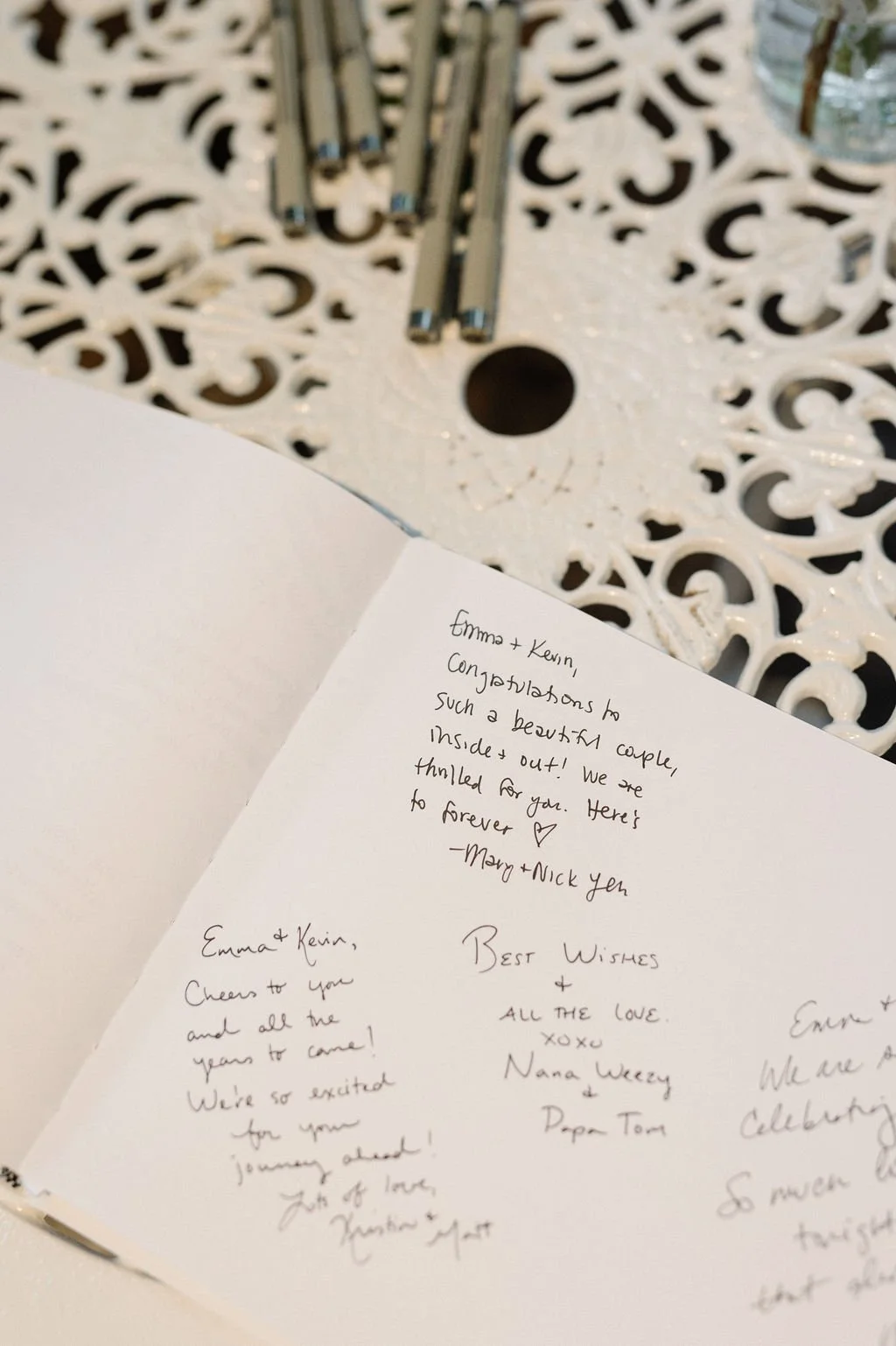 Open greeting card with handwritten messages on a white surface, next to a decorative white table with metallic rods on top.