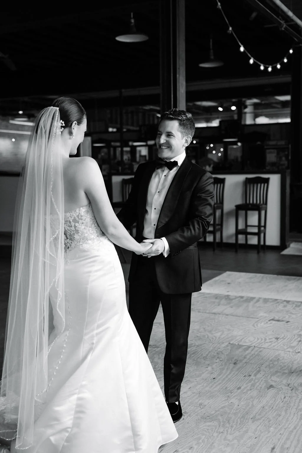 A bride and groom holding hands and smiling during their wedding ceremony in a decorated venue.