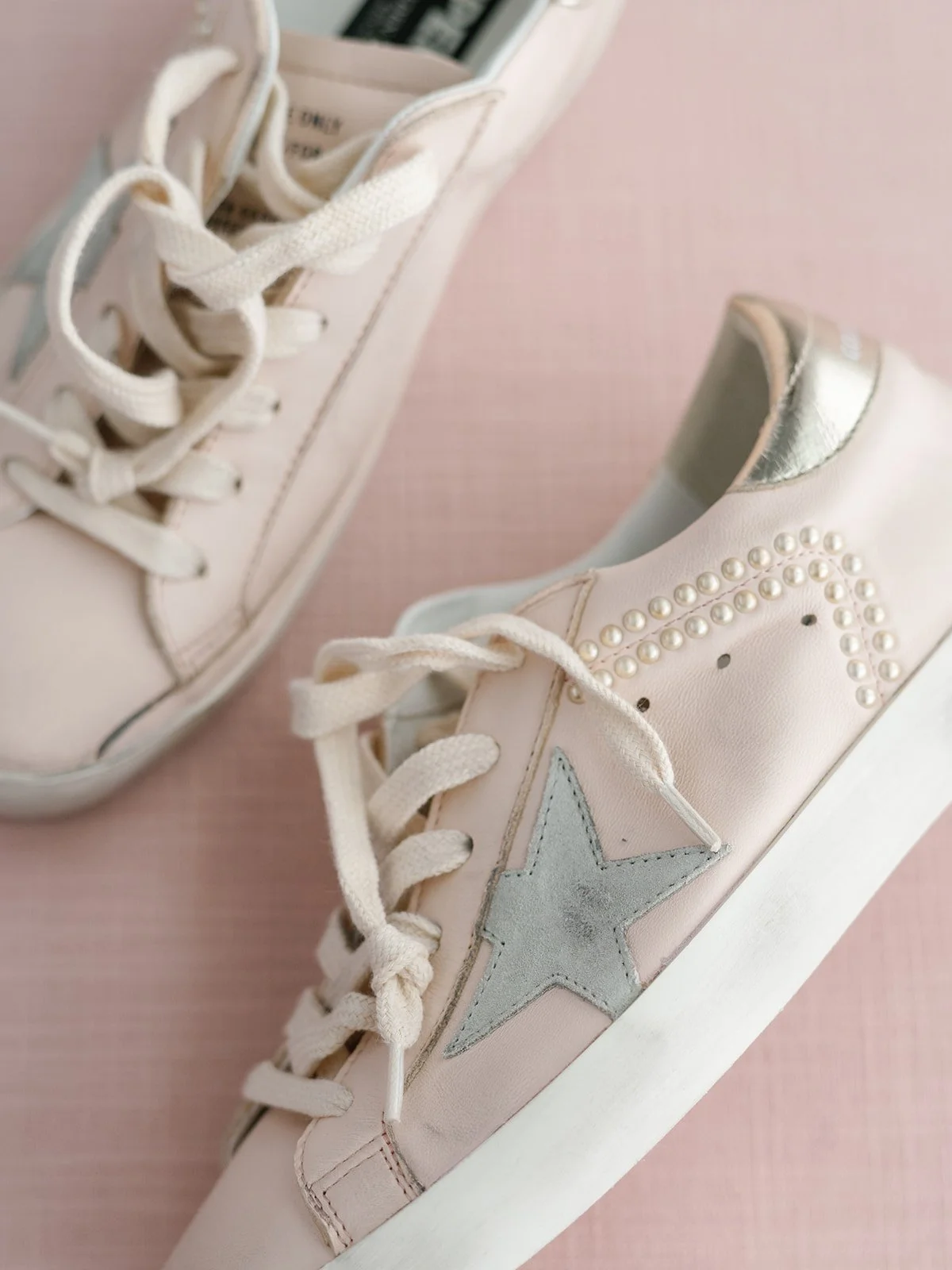 Close-up of pink sneakers with star and pearl embellishments on a pink background.