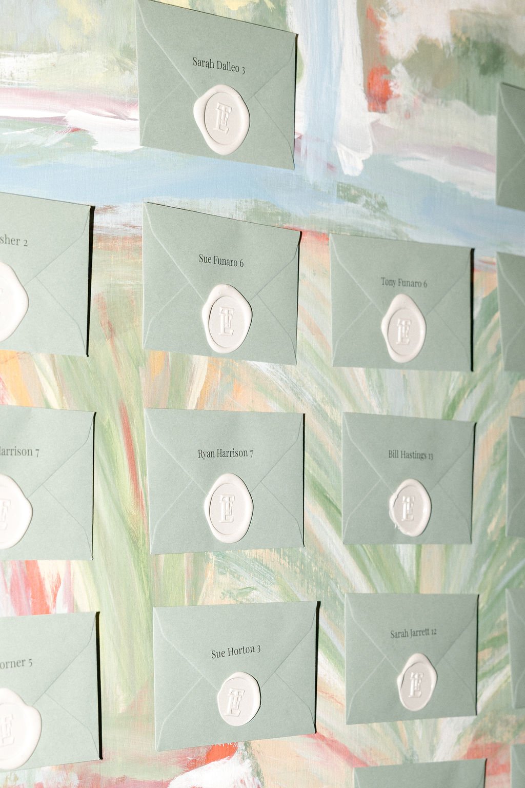 Light green envelopes with white wax seals and printed names, attached to a colorful, abstract painted background.