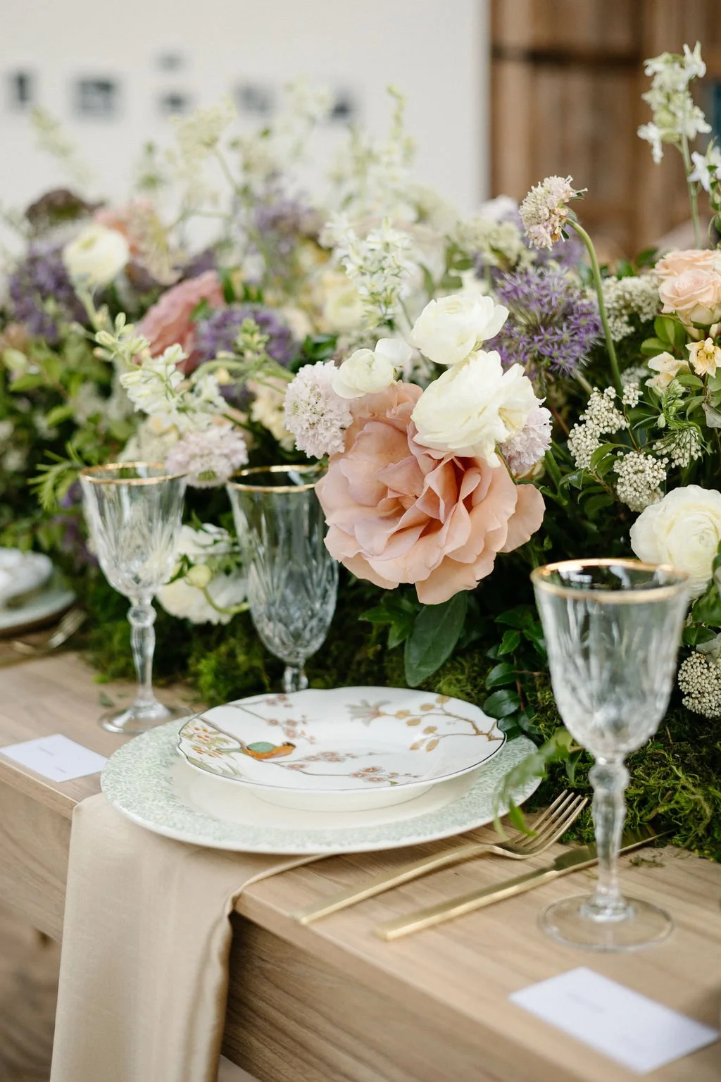 Elegant table setting with floral centerpiece, gold-rimmed glasses, decorative plates, and gold cutlery on a wooden table.
