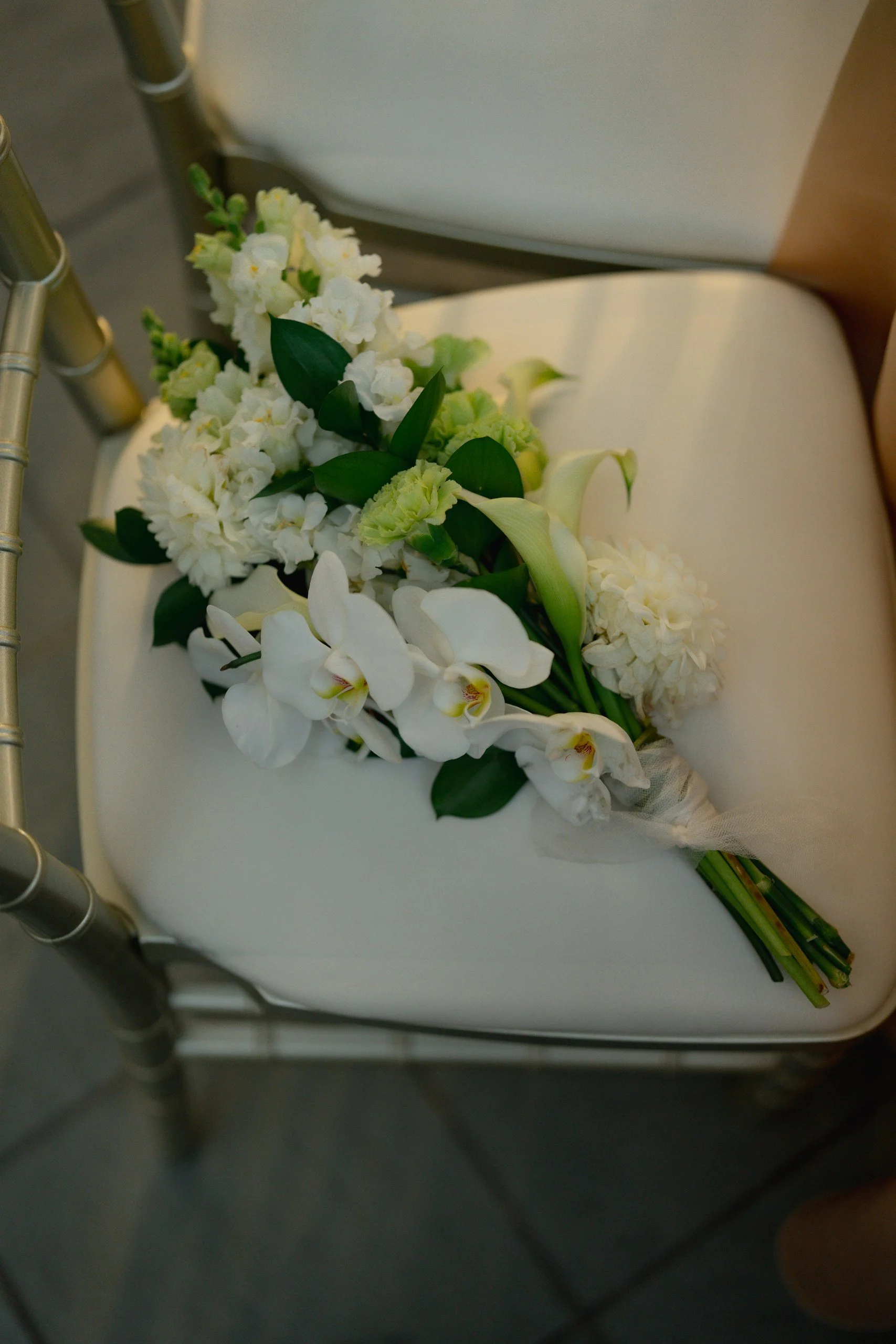 A bouquet of white flowers, including orchids and lilies, resting on a white chair.