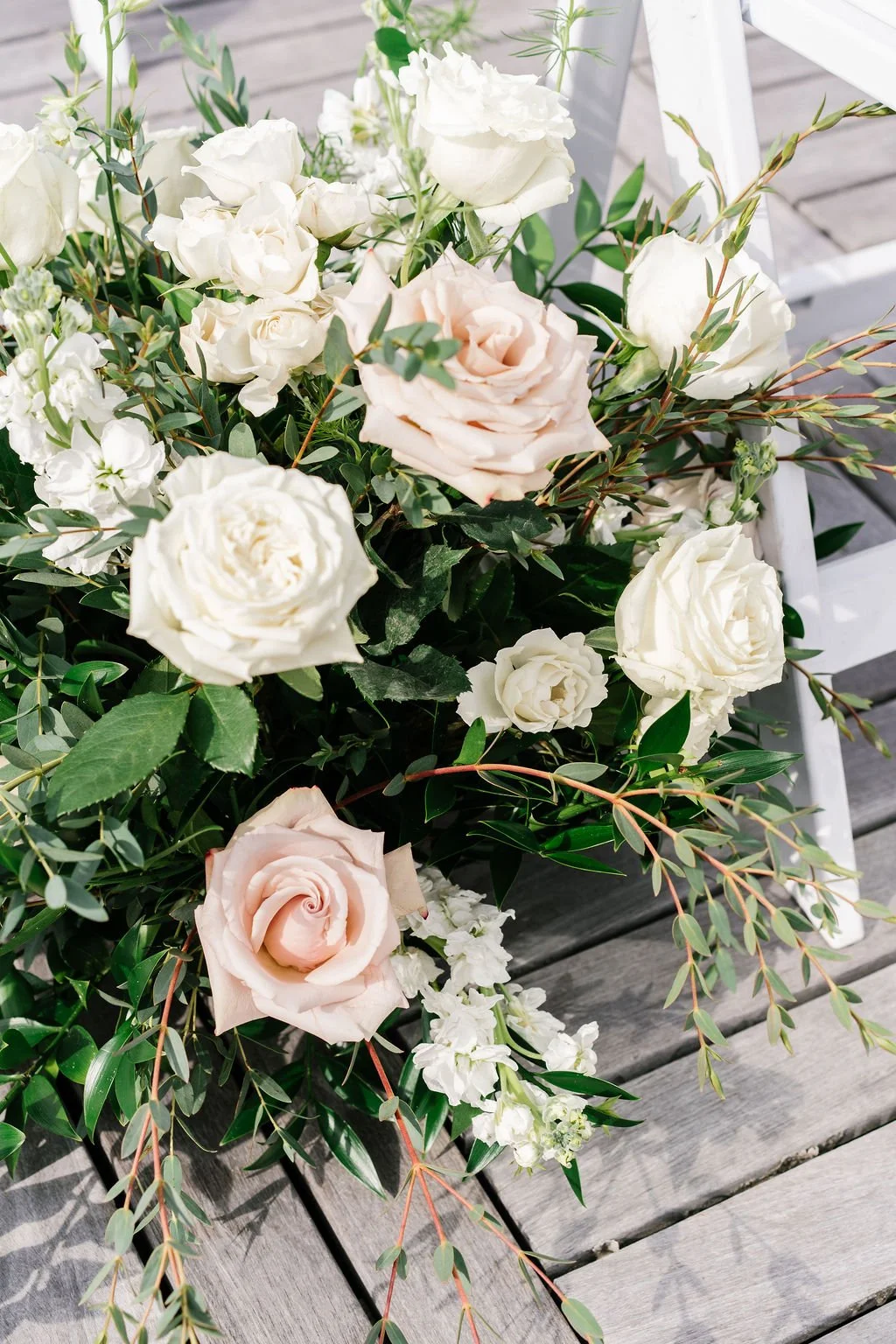 A bouquet of white and pale pink roses and greenery resting on a wooden surface.