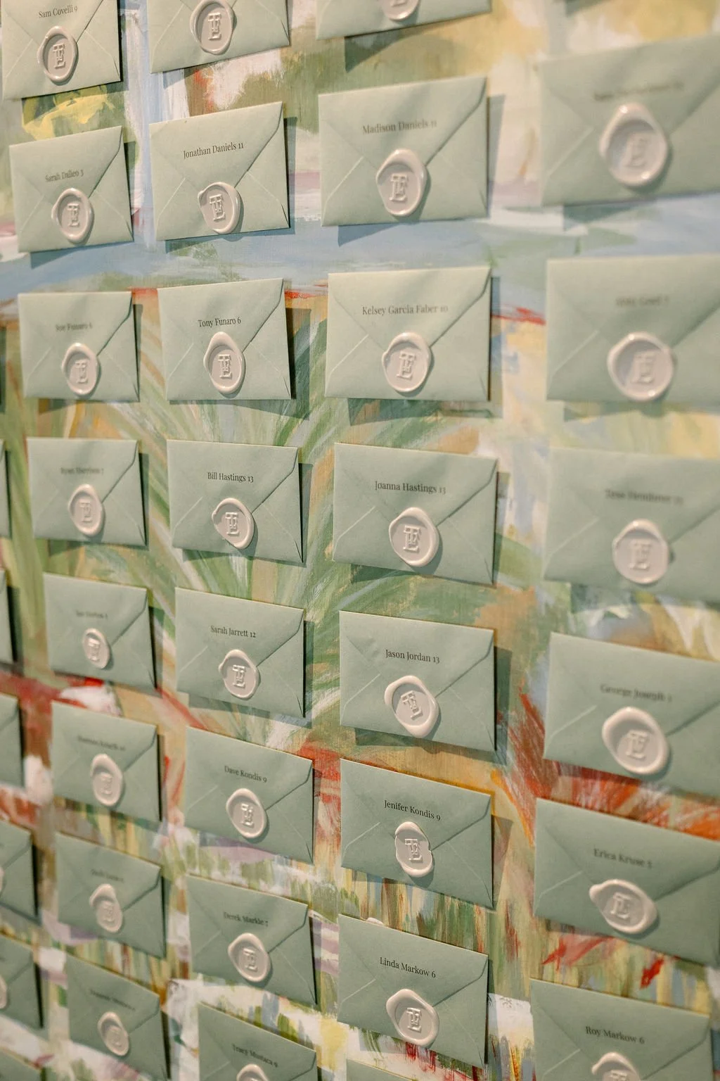 A wall with multiple light green envelopes sealed with wax seals, each containing different names.
