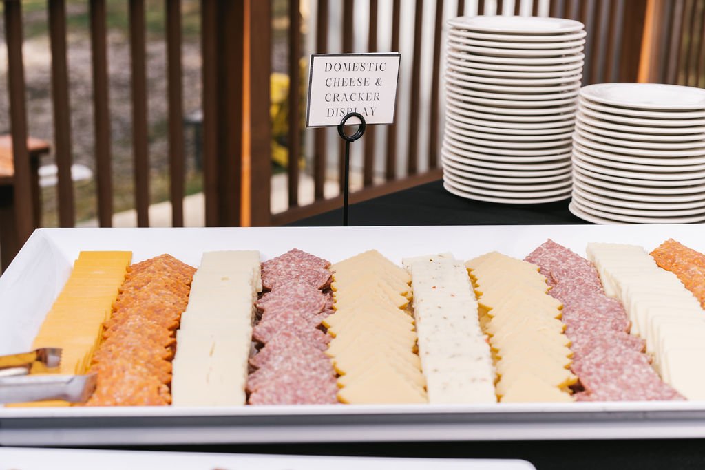 Tray of sliced cheeses and cold cuts on a table at a domestic cheese and cracker display.