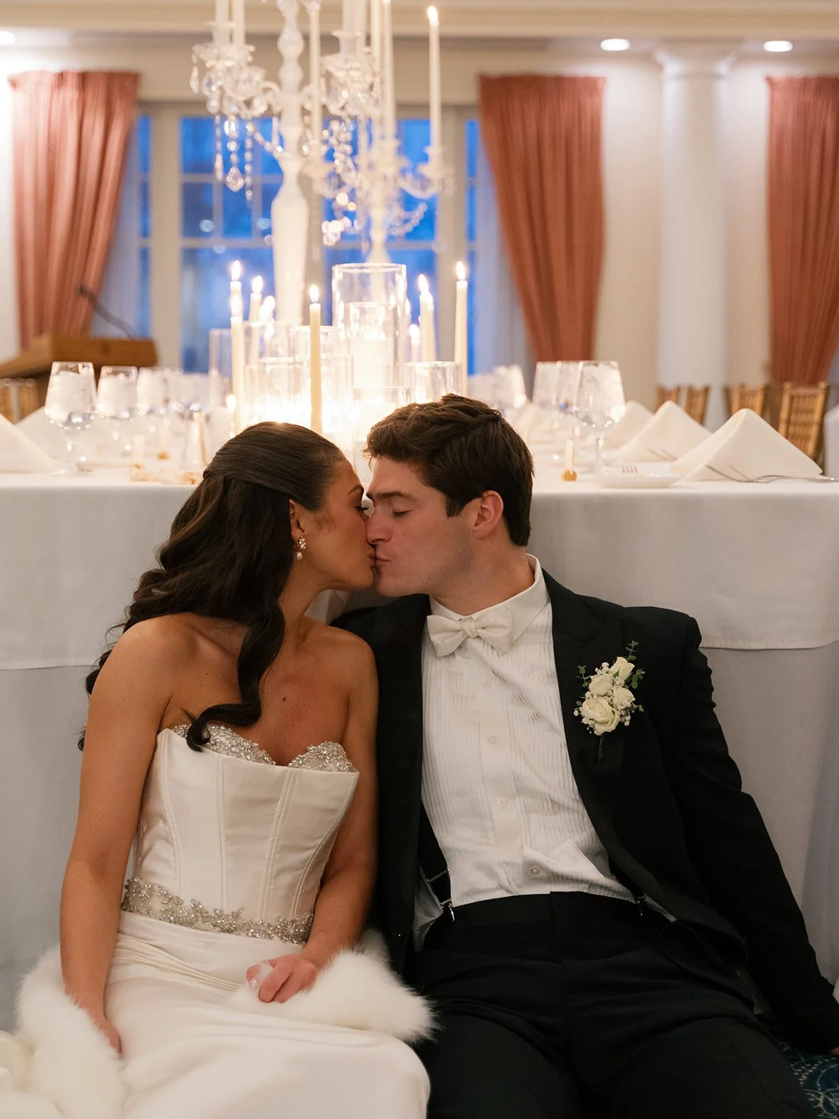 A bride and groom sharing a kiss at their wedding reception, with a decorated table and candelabras in the background.