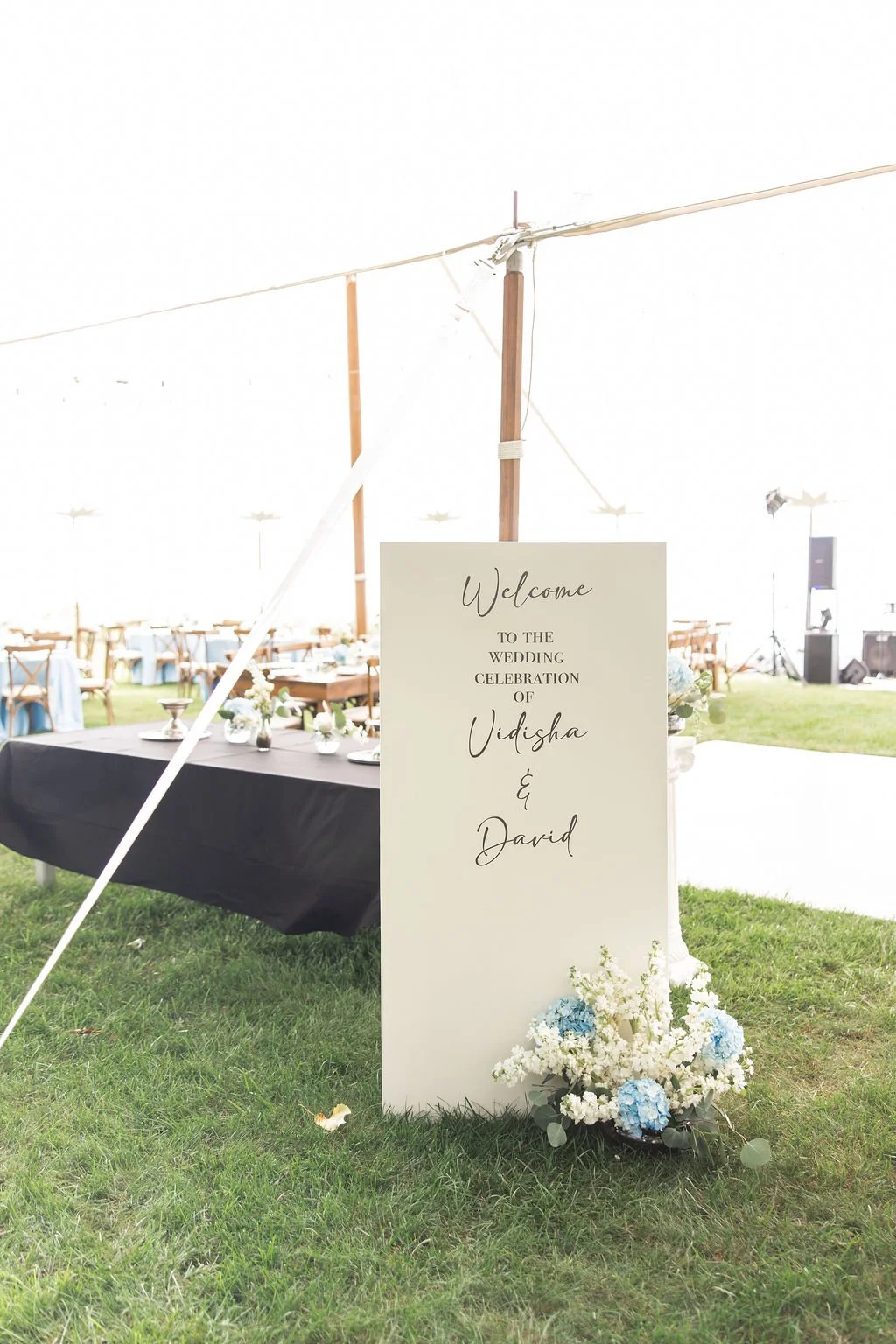 Wedding welcome sign for Vidisha and David with floral decoration at an outdoor celebration tent.