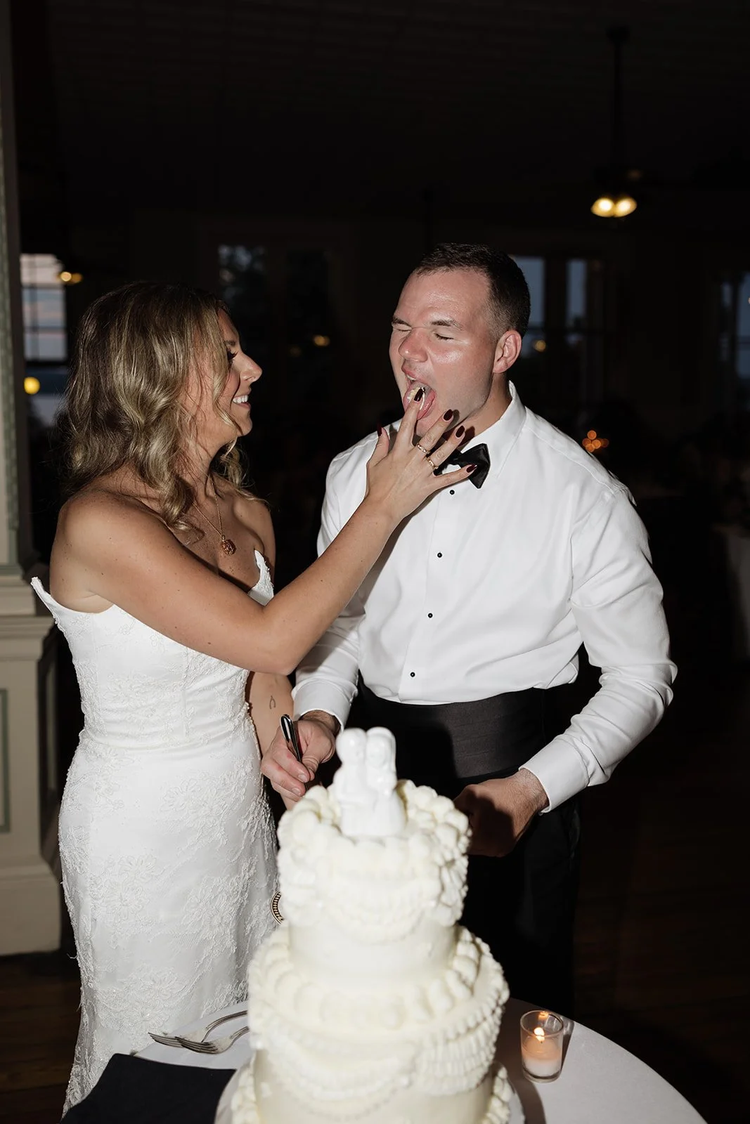 Bride playfully feeding groom wedding cake at reception.