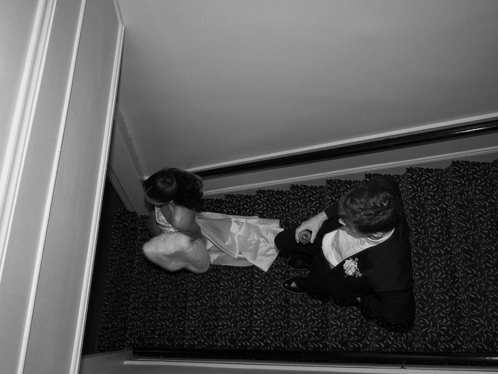 A bride in a wedding dress and a groom in a suit are standing in an elevator, viewed from above.