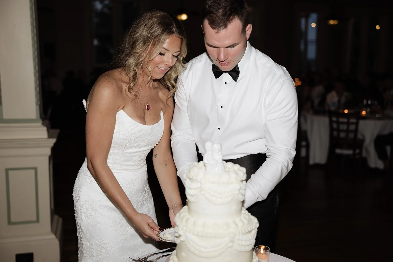 A bride and groom in formal attire cutting a wedding cake together at their reception.