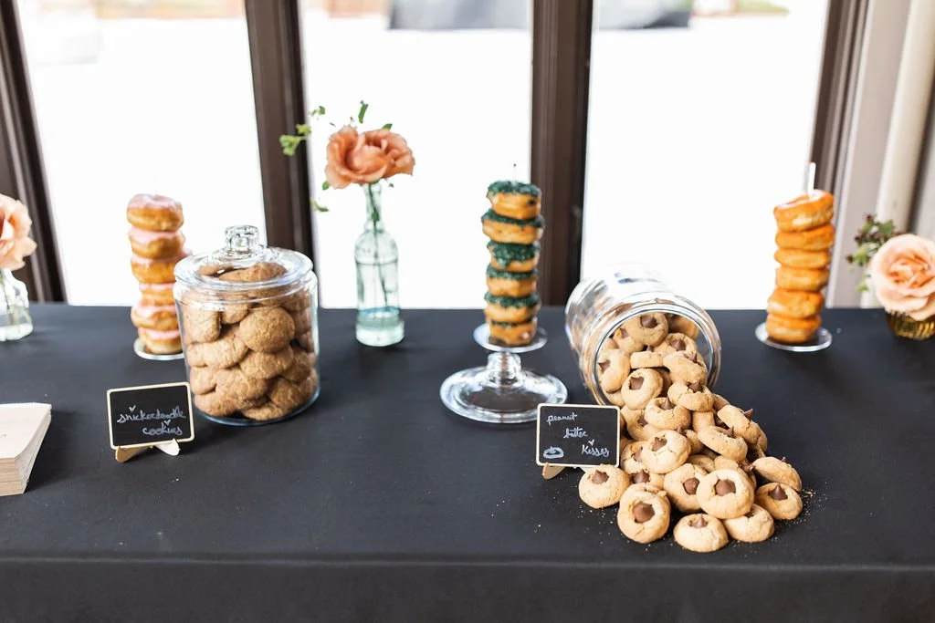 Table with cookies, cupcakes, and flowers at a party or event.