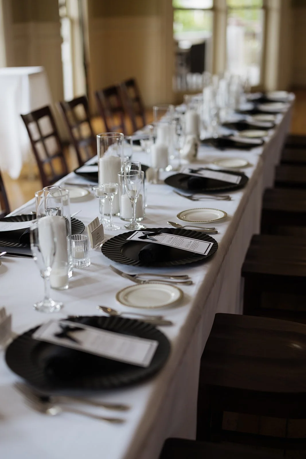 A long banquet table set for a formal event, with black and white dinnerware, glassware, candles, and place cards, arranged in an elegant dining setting.
