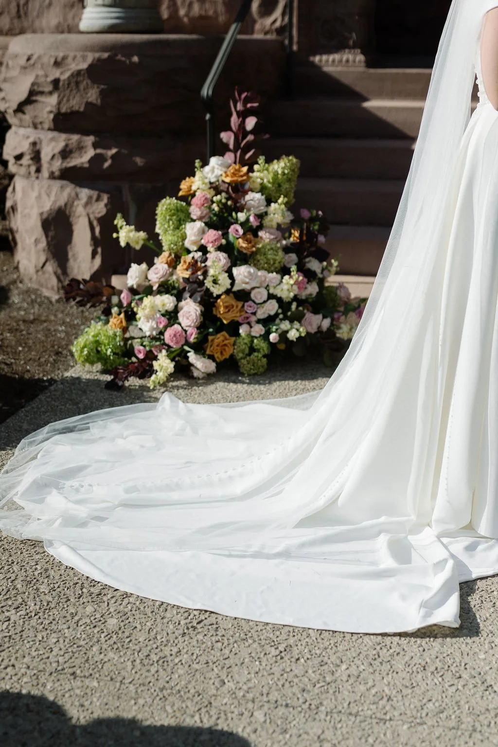 A wedding dress with a long train beside a floral arrangement of pink, white, and yellow flowers.