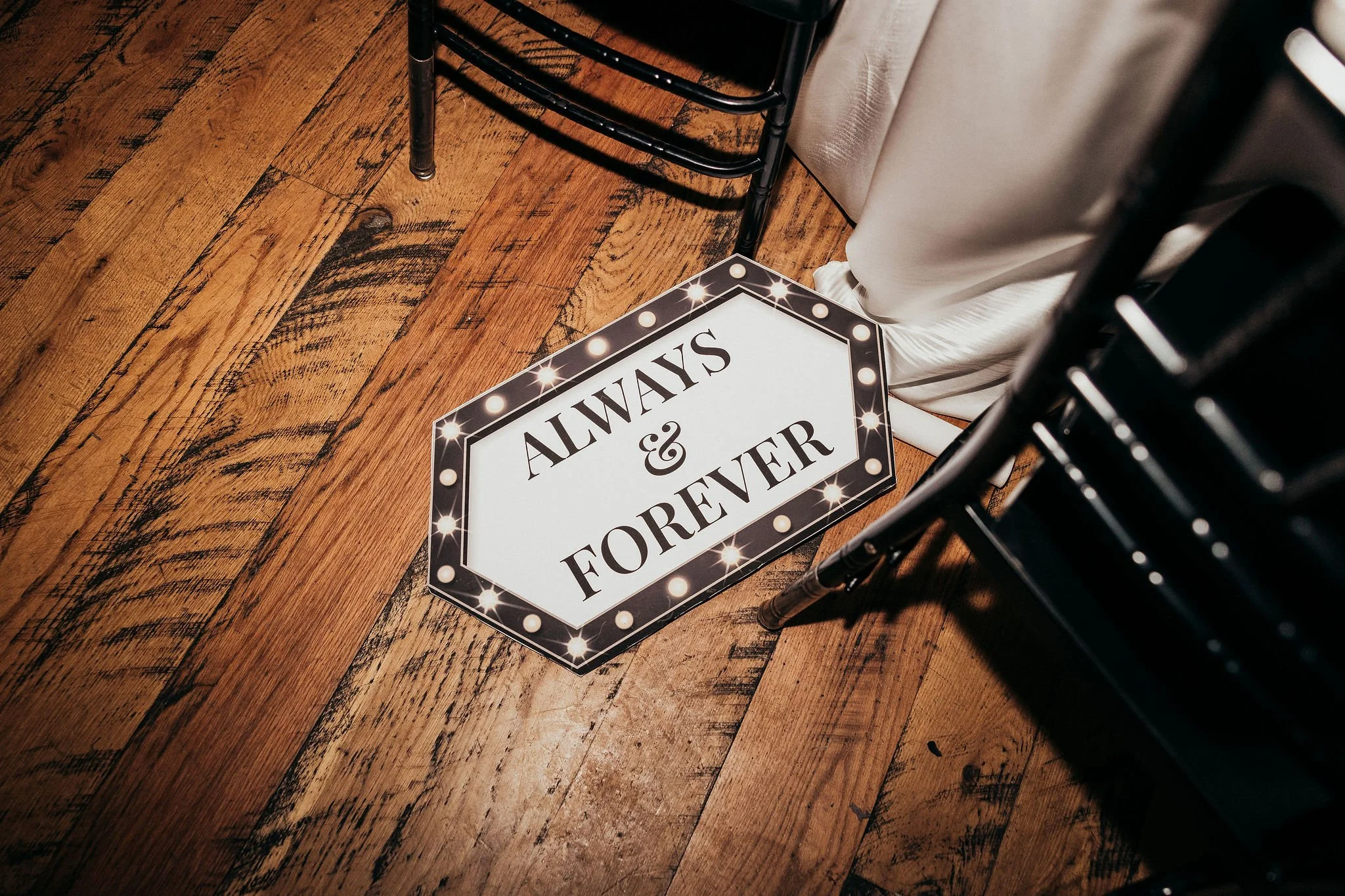 A tabletop with a black chair, a white curtain, and a decorative sign that reads 'Always & Forever' on the wooden floor.