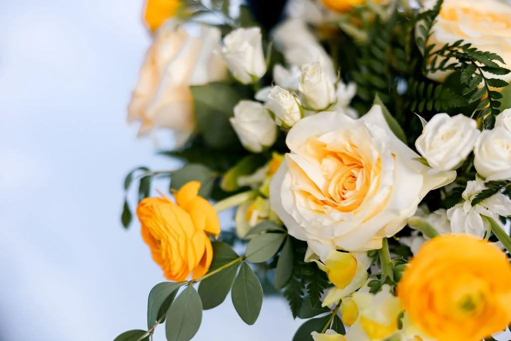 A bouquet of white and yellow roses with green leaves.