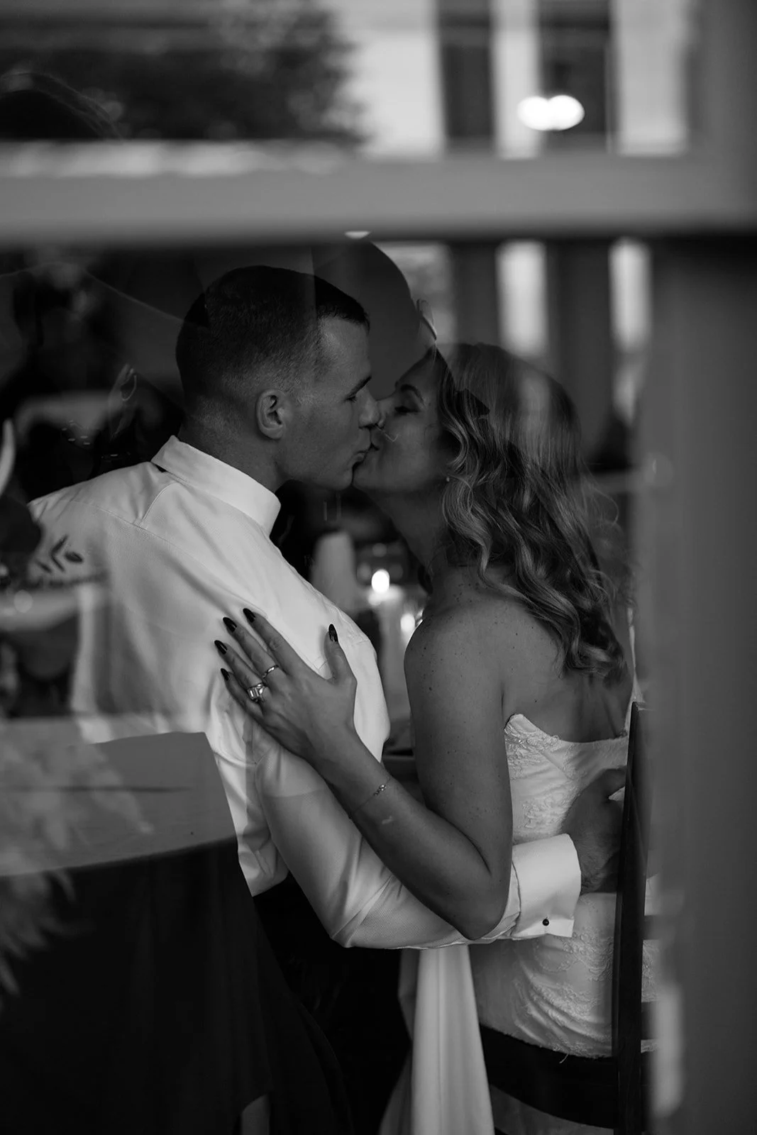 A couple sharing a kiss through a glass window, with the woman’s hand on the man’s chest, in black and white.