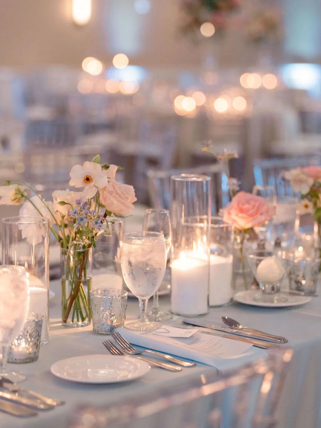 Elegant banquet table decorated with pink and white flowers, candles, and glassware for a formal event.
