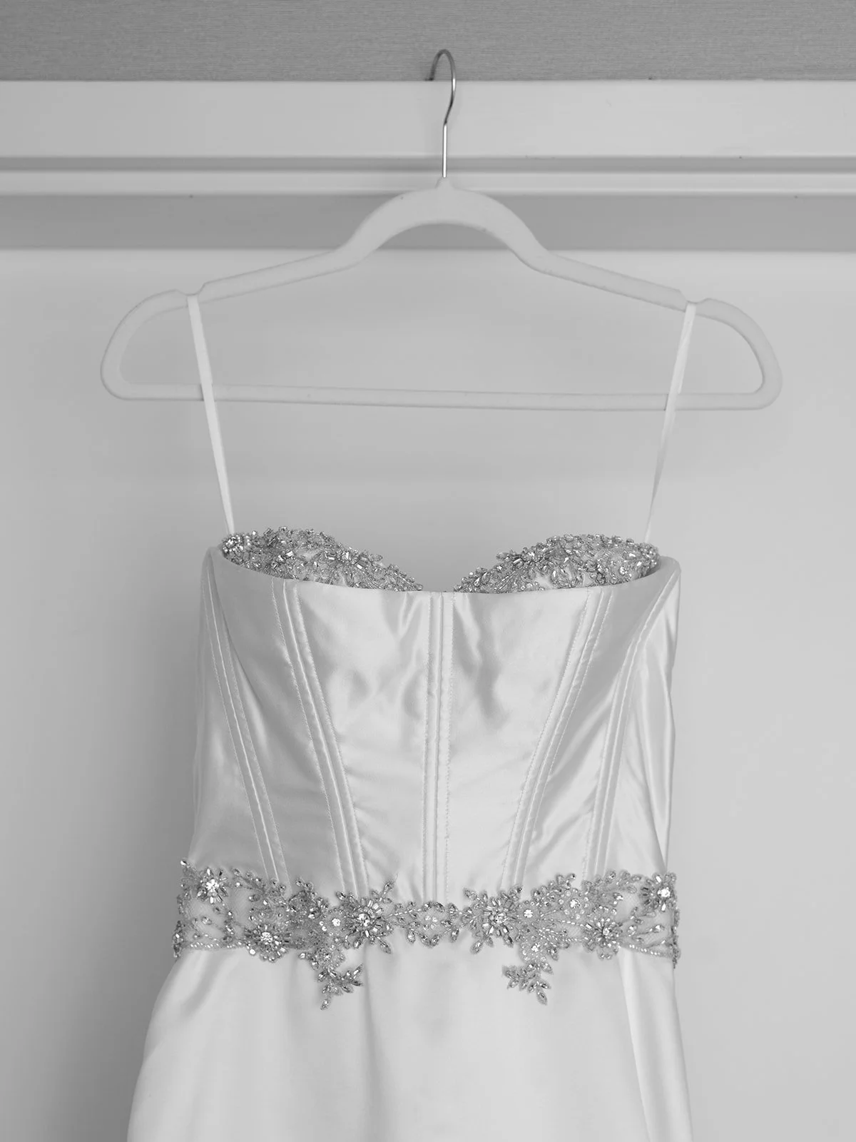 Elegant white wedding dress with beaded embellishments, hanging on a white hanger against a plain background.