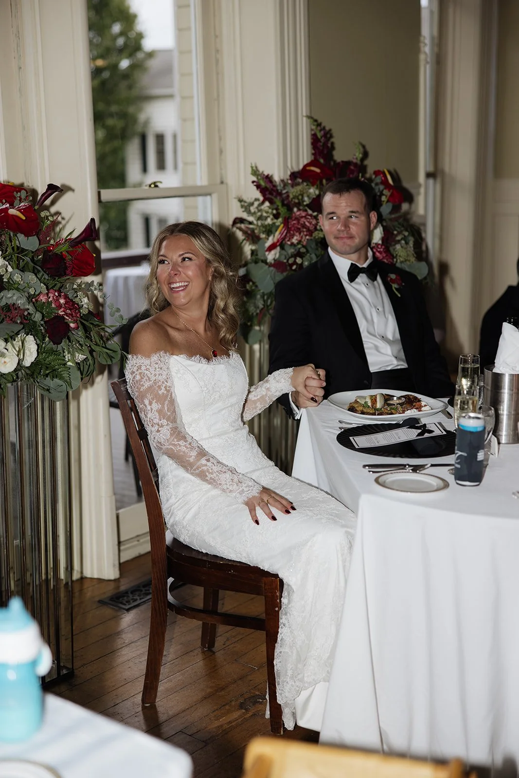 A bride and groom sitting at a banquet table holding hands during their wedding reception, smiling and looking content.