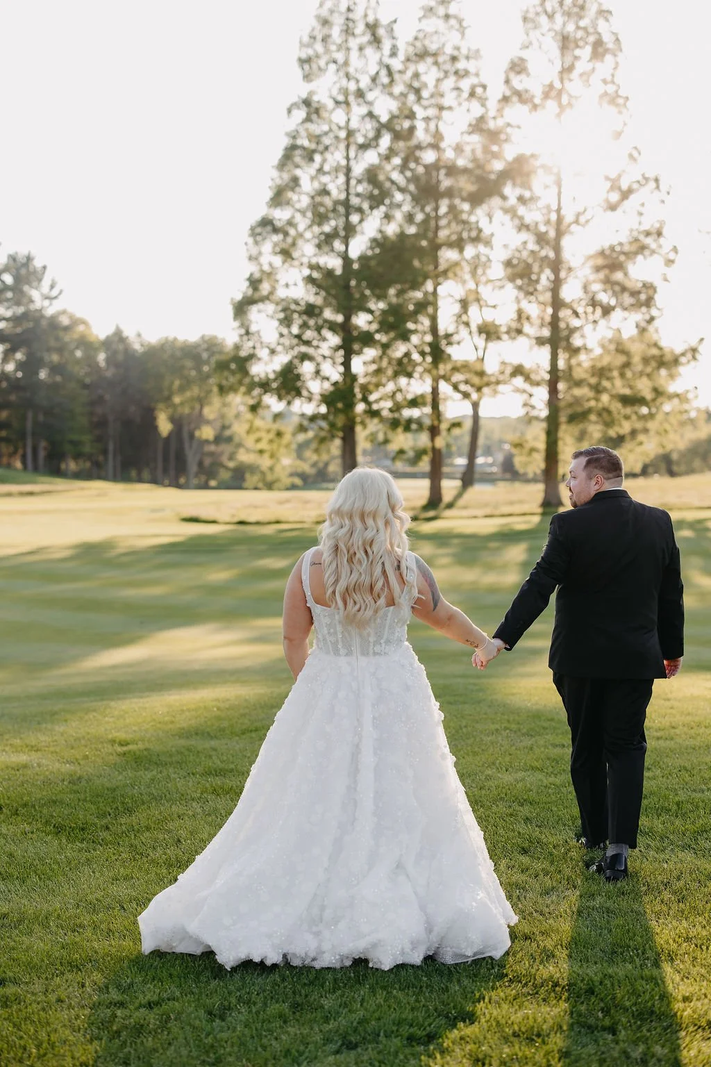 A bride and groom walking hand in hand on a grassy field during sunset.