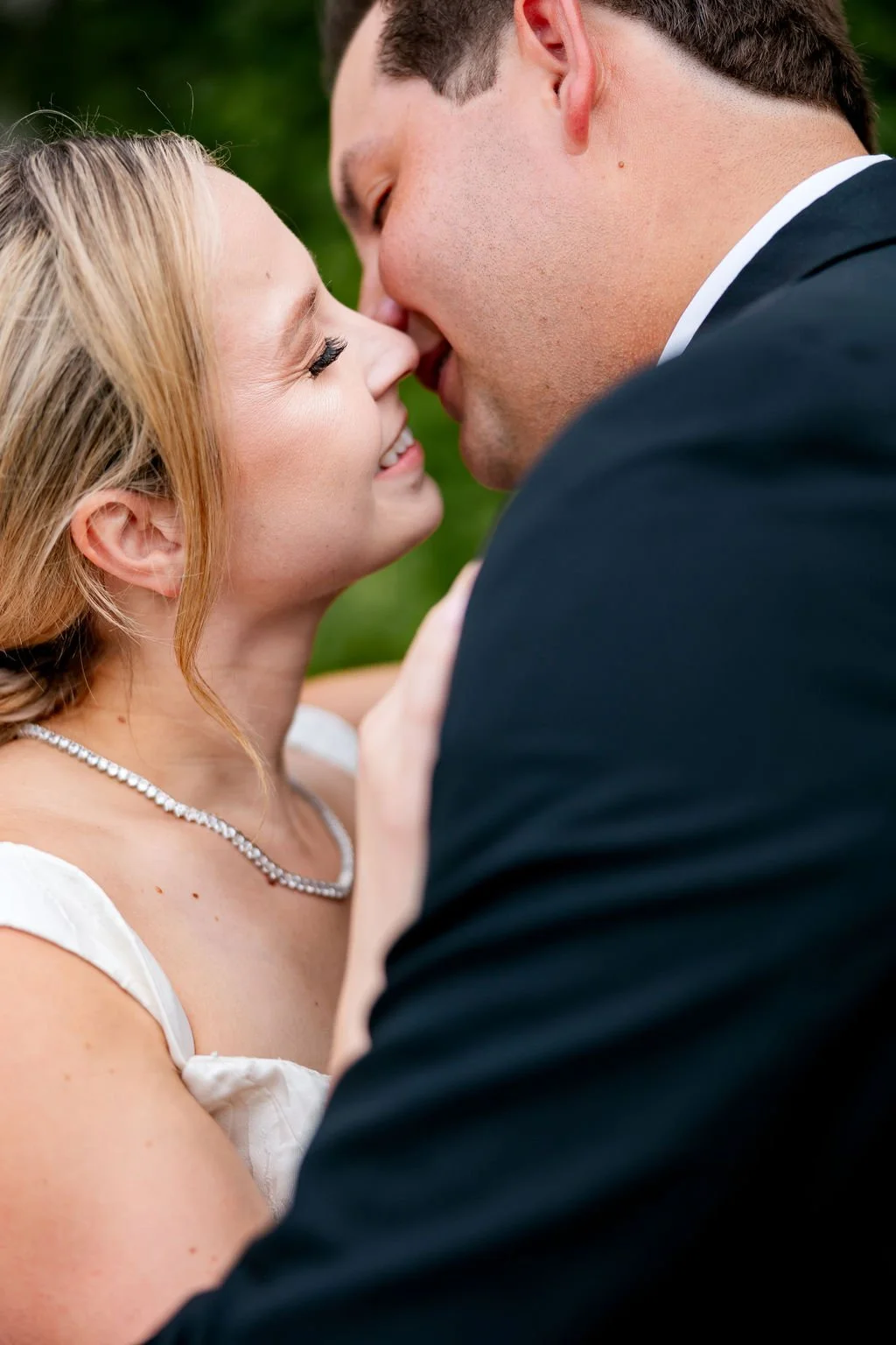 A close-up of a couple outdoors, about to kiss, with a green blurred background.