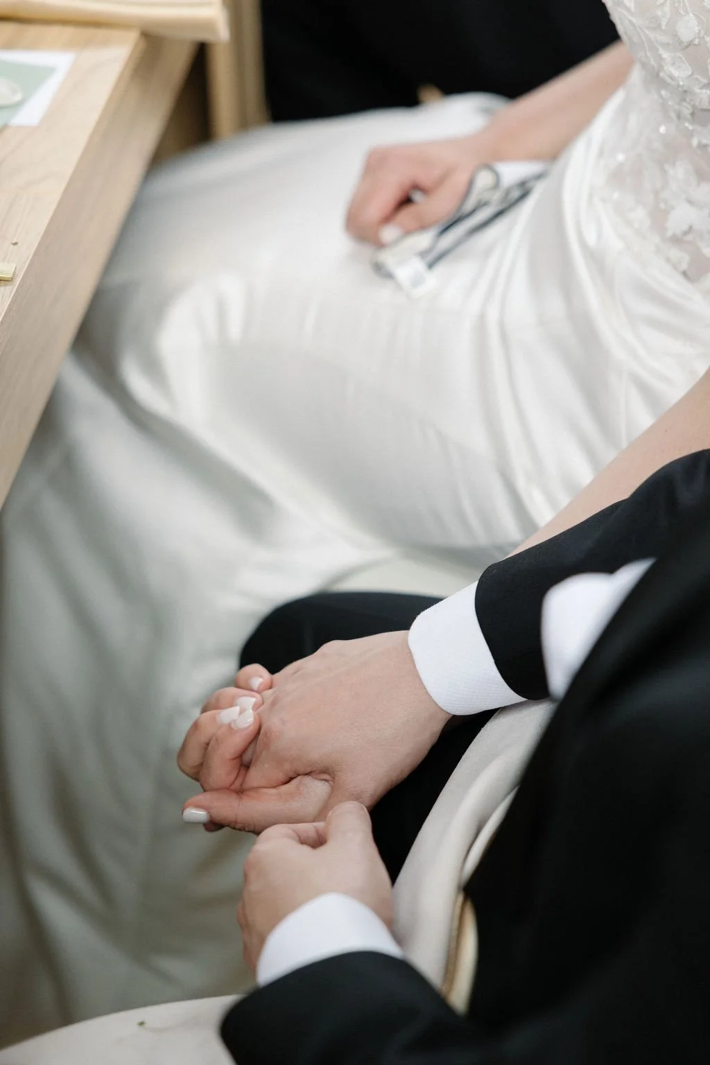 A close-up of a bride and groom holding hands during a wedding ceremony, with the bride wearing a white dress and the groom in a black suit.