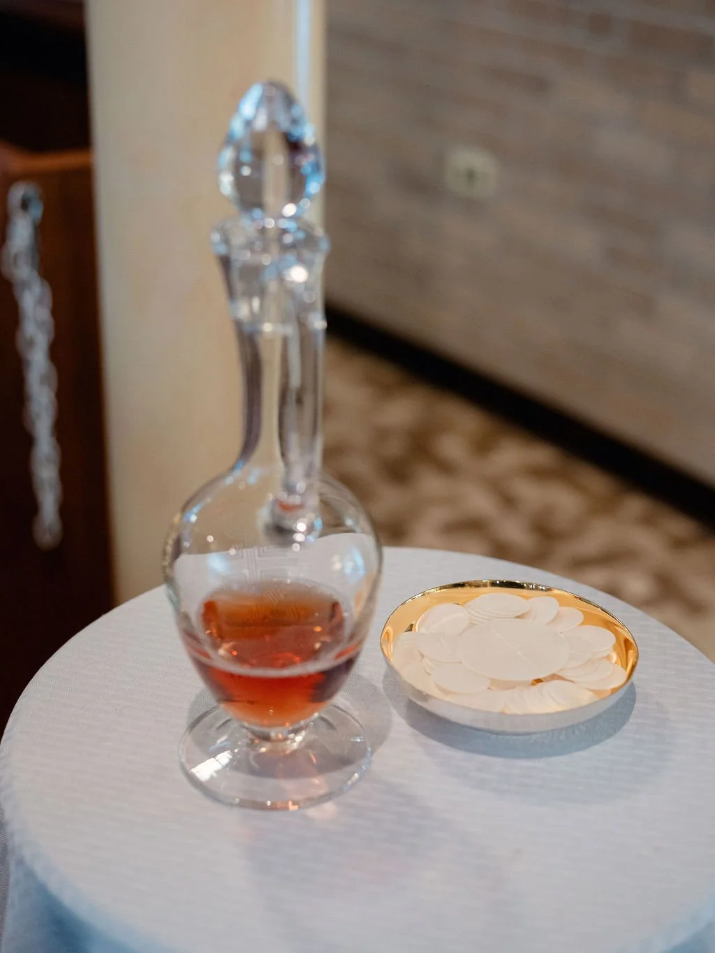 A decanter with a small amount of pinkish liquid and a bowl of white coasters on a white tablecloth.
