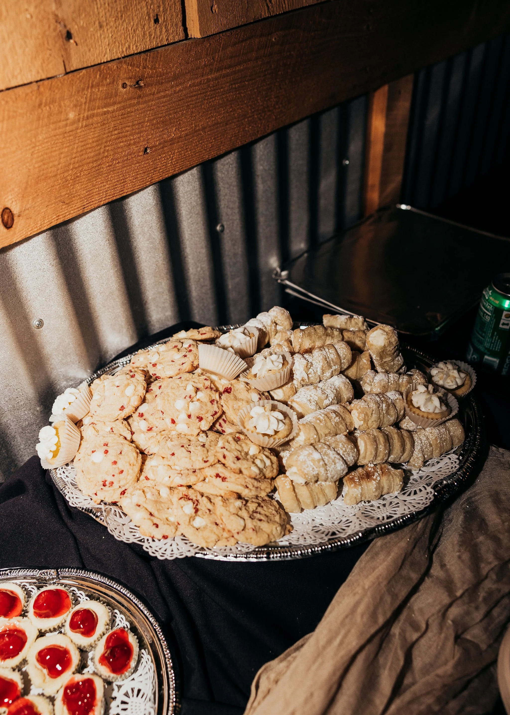 Assorted cookies and pastries on a silver tray decorated with a white paper doily, set on a black tablecloth at a dessert display.
