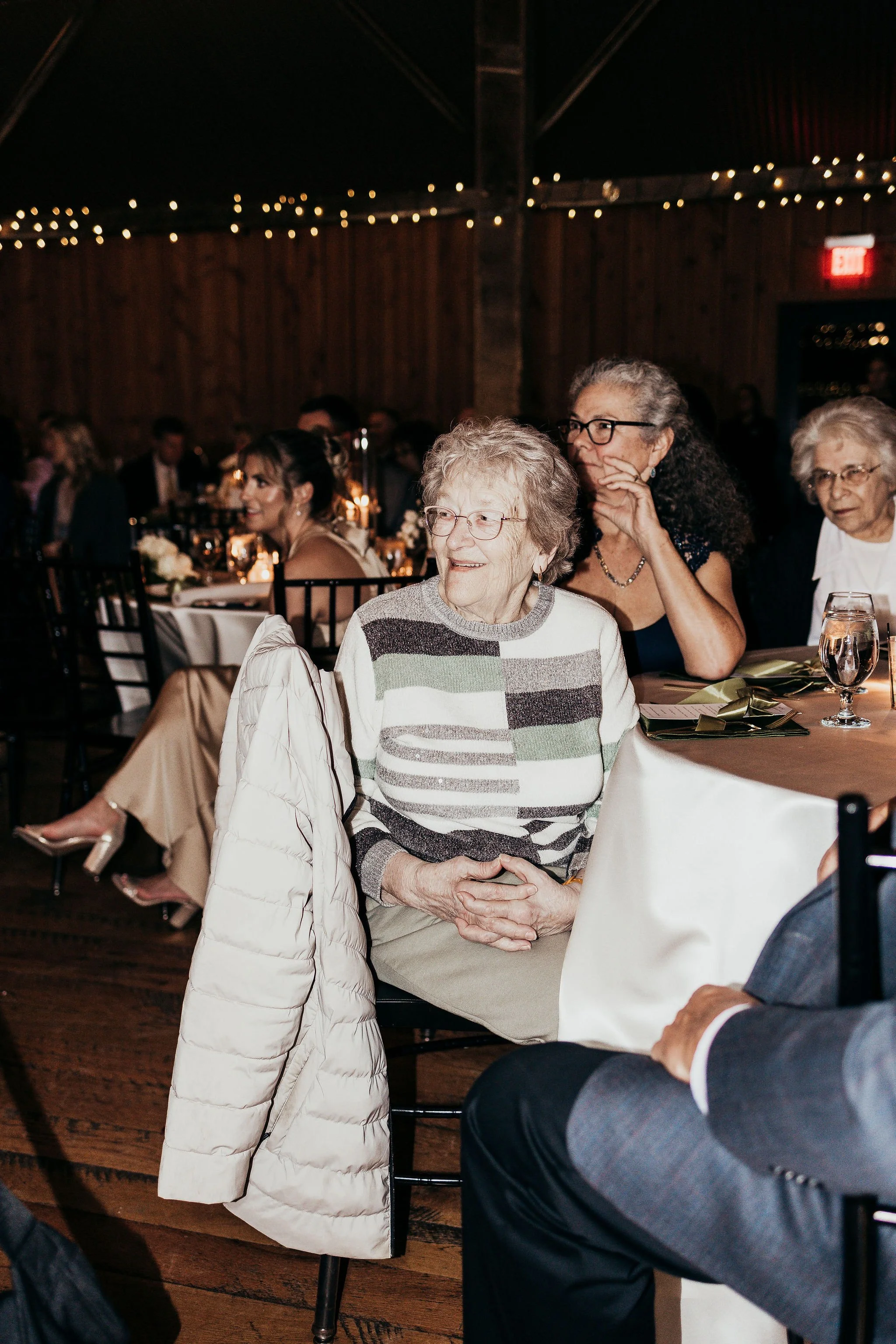 People sitting at a dinner event with warm lighting, wooden walls, and fairy lights overhead.