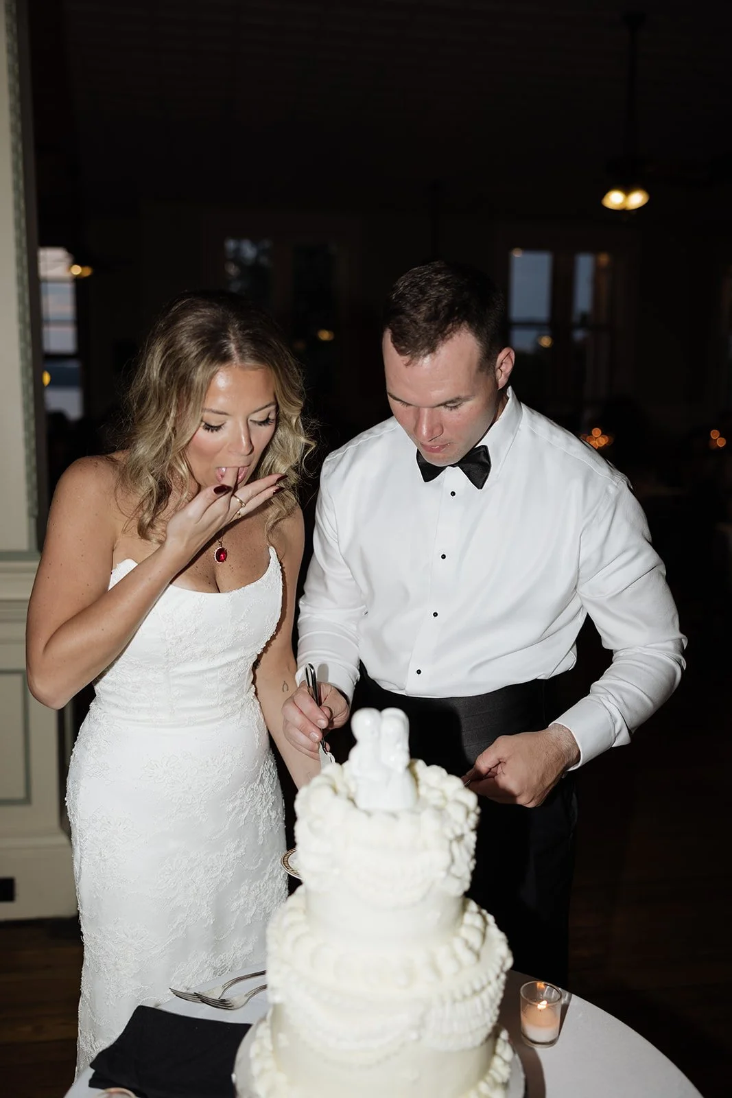 Bride and groom cutting their wedding cake at reception, with a wedding cake decorated with white frosting and figurines on top.