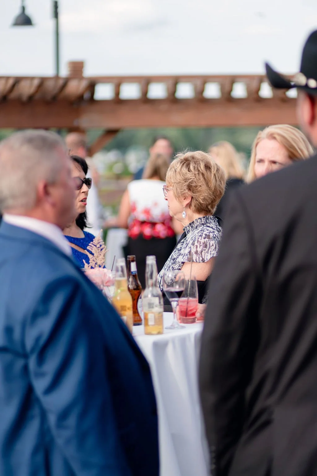 People talking at an outdoor social event with drinks and a wooden pergola in the background.