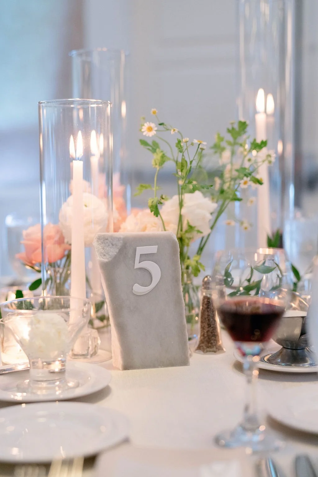 Elegant table setting at a wedding or formal event with candles, floral arrangements, a table number 5 card, and glasses of wine.