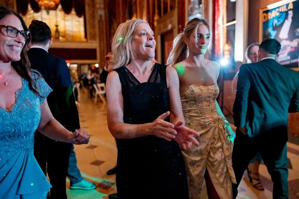 People dancing and socializing at an indoor event or party, with wooden walls and colorful lighting.