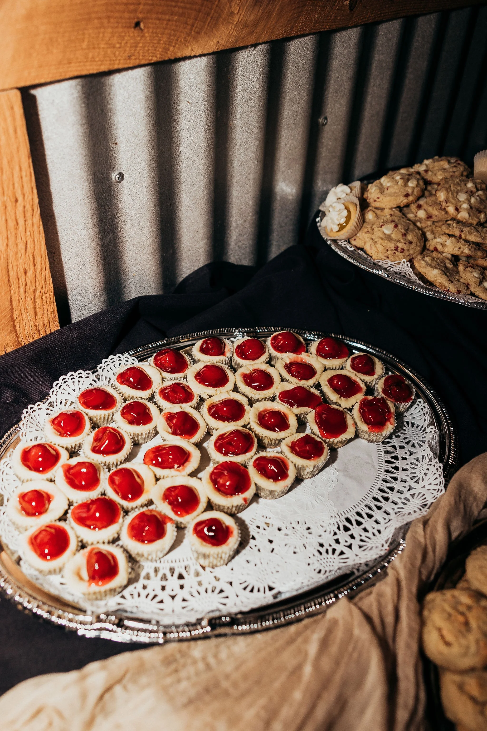 Tray of mini cheesecakes with cherry topping and a plate of oatmeal cookies visible in the background.