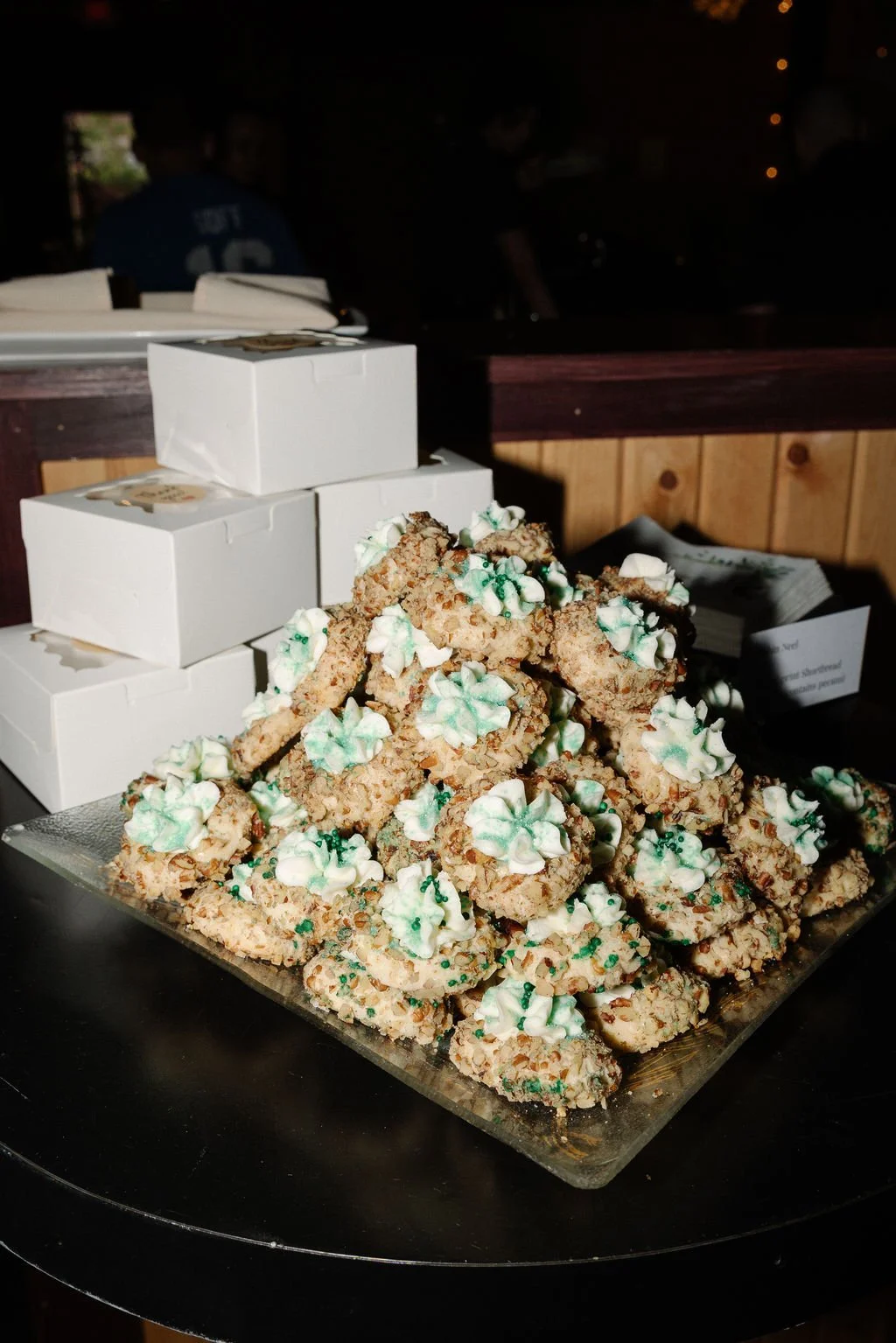 Stacked rice cereal treats decorated with green and white icing and green sprinkles, with white boxes in the background.