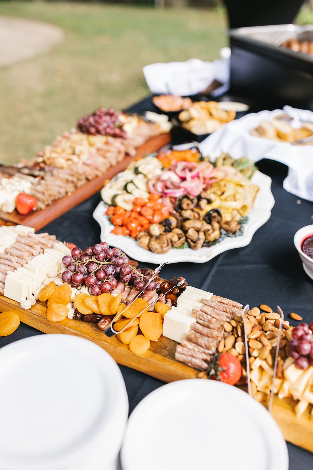 Charcuterie board with cheeses, grapes, dried apricots, and meats, with a vegetable platter in the background.
