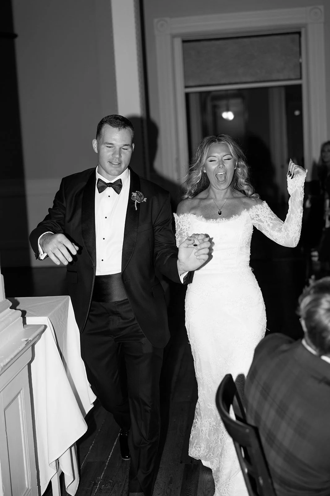 A couple dressed in formal wedding attire dancing at their wedding reception. The groom wears a tuxedo, and the bride wears a lace wedding dress, both smiling and enjoying the moment.