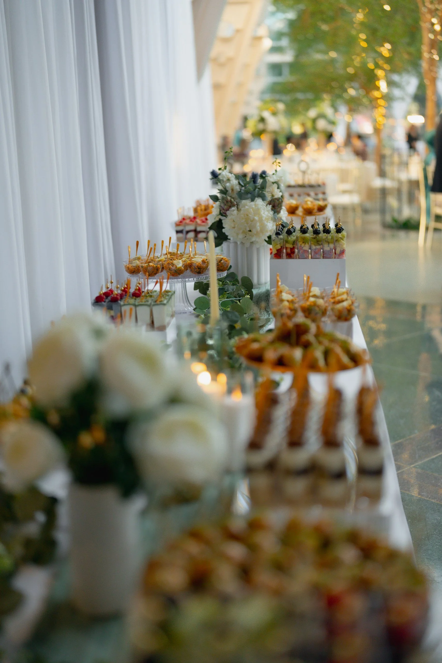 A dessert table with an array of colorful sweets and pastries, including fruit-topped treats, amidst floral decorations on a white tablecloth during a celebration or event.