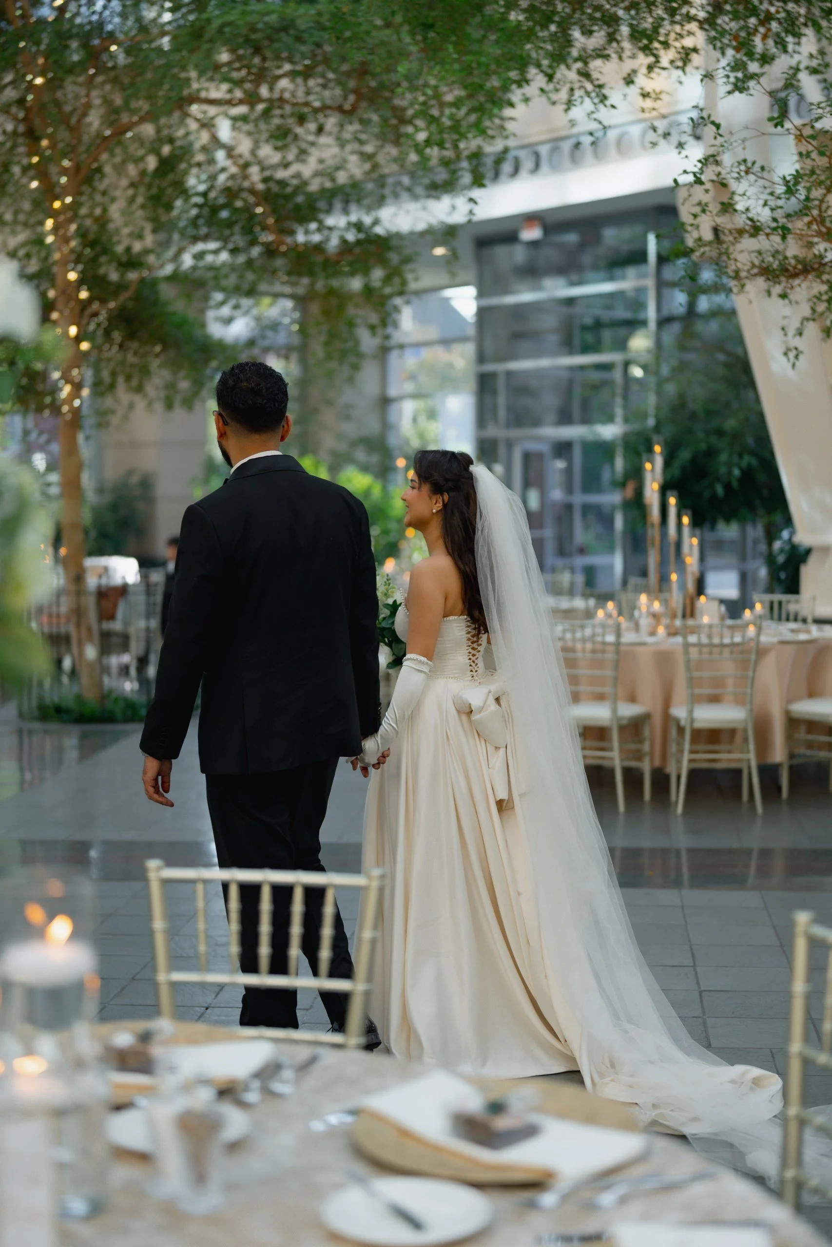 A bride and groom standing together during their wedding reception in a decorated indoor venue with tables and trees.