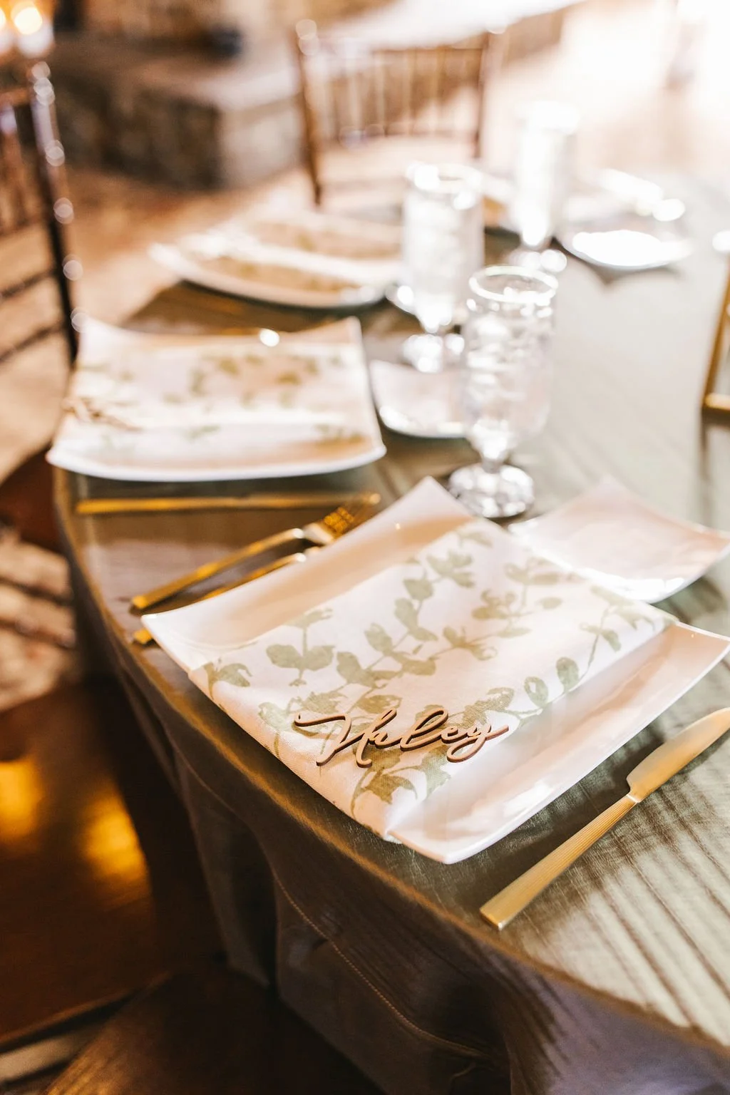 Elegant dining table set with floral napkins, gold utensils, wine glasses, and water glasses, with a decorative table name card reading 'Chloe' in a cozy restaurant.