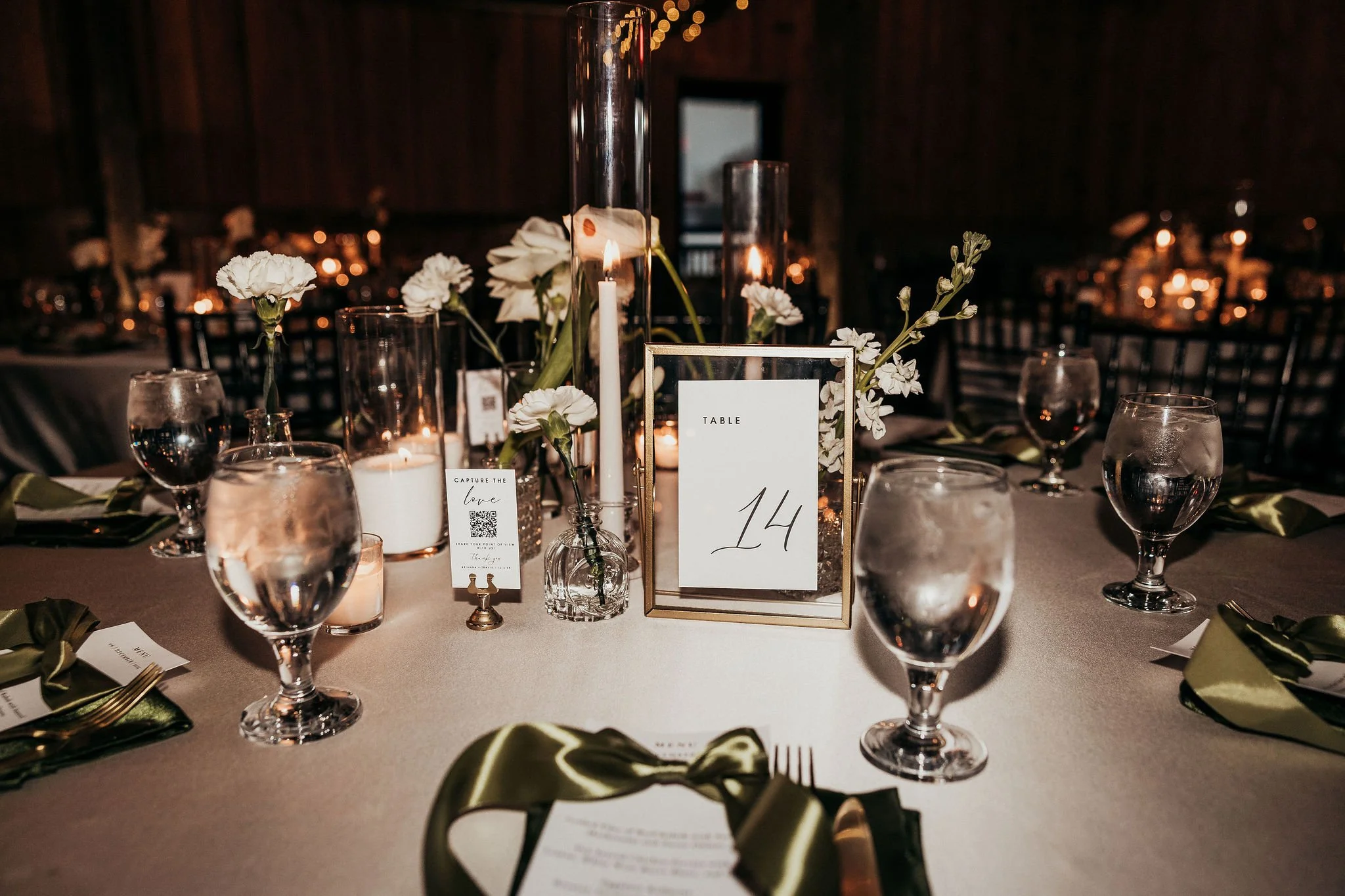 A decorated table set for a wedding or special event with white flowers, candles, and a table number card, in a dimly lit venue.