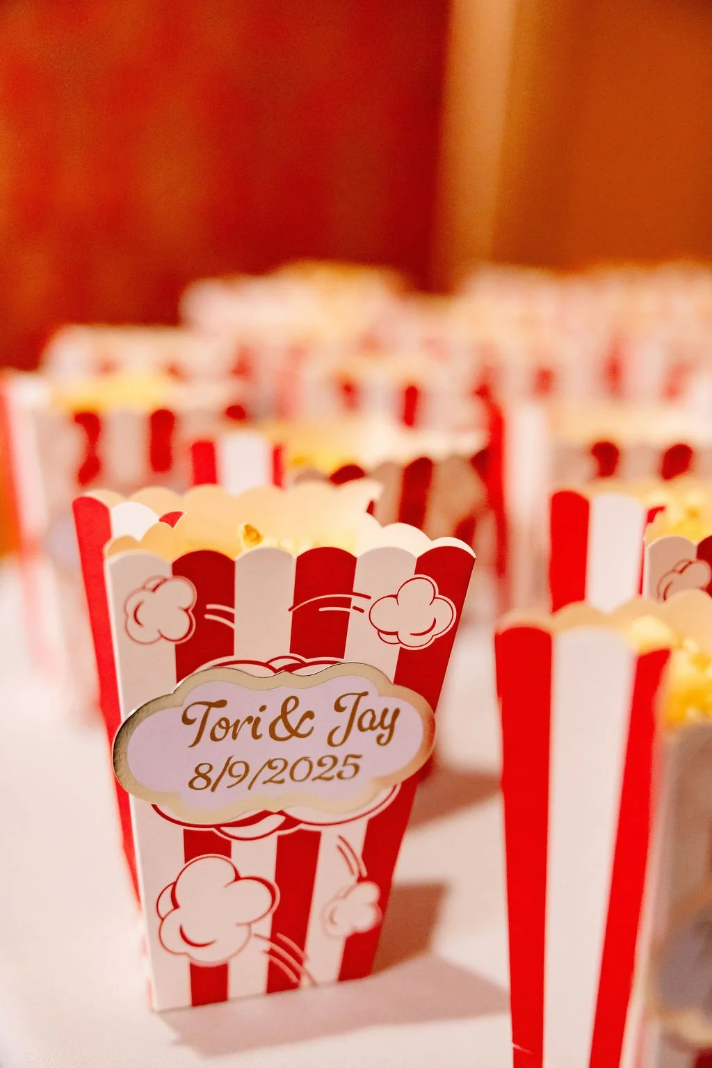 Close-up of decorative popcorn boxes with red and white stripes, featuring names 'Tori & Jay' and date '8/9/2025', at an event or celebration.