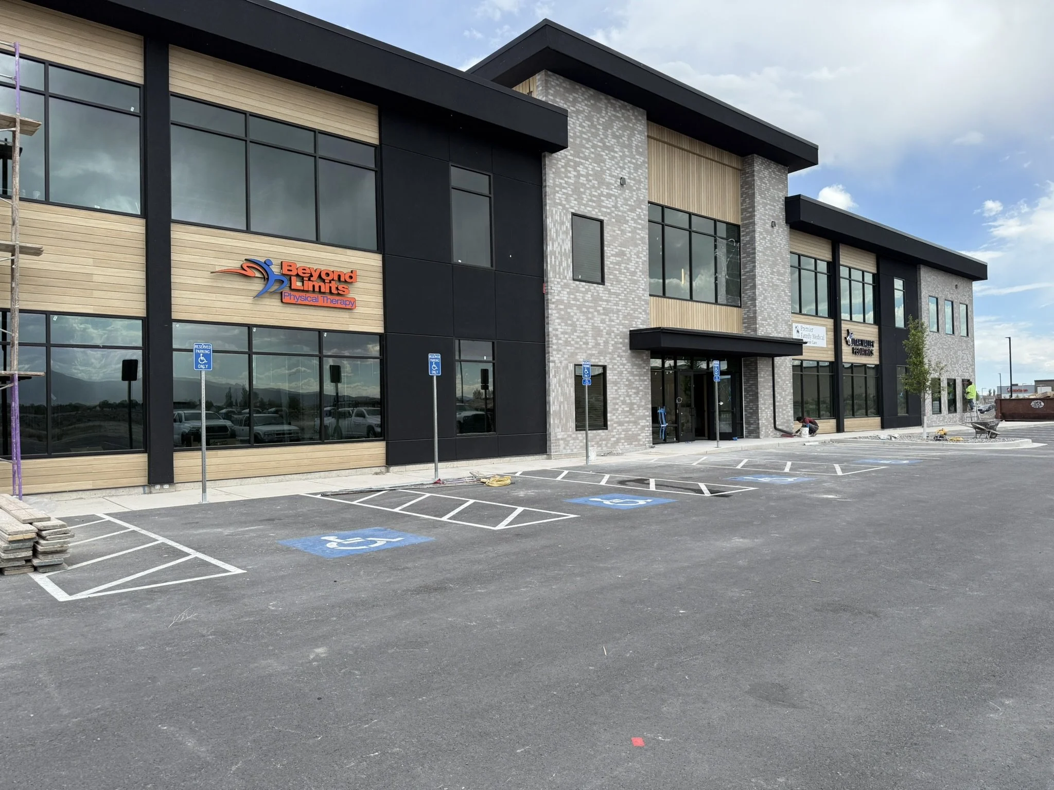Modern two-story commercial building with large glass windows and a parking lot in the foreground with painted handicap parking spaces.