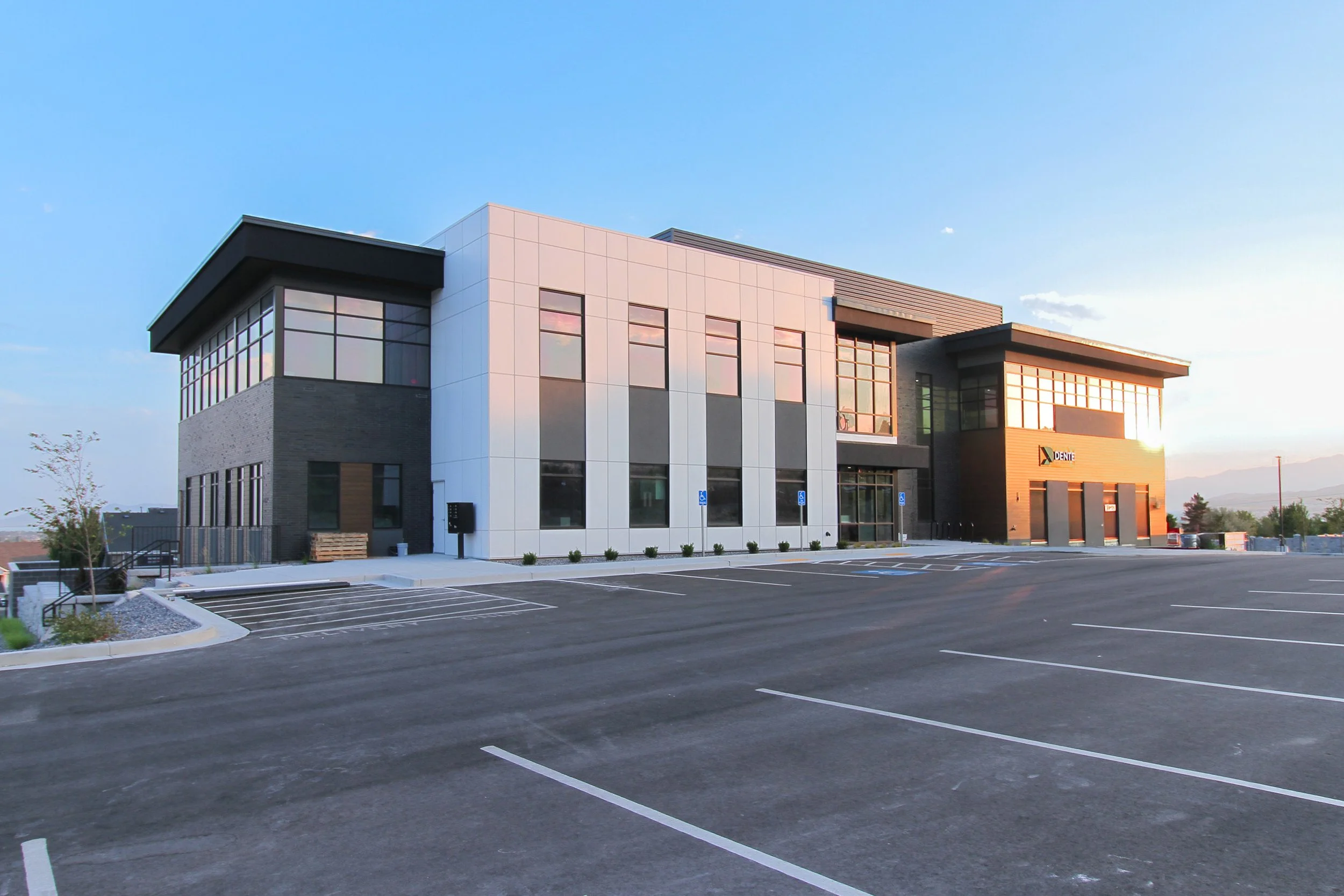 Modern commercial building with large windows and parking lot in front, under a clear sky at sunset.
